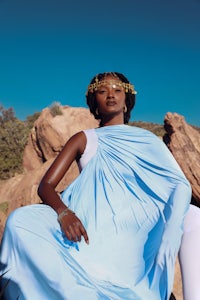 a woman in a blue dress sitting on top of rocks